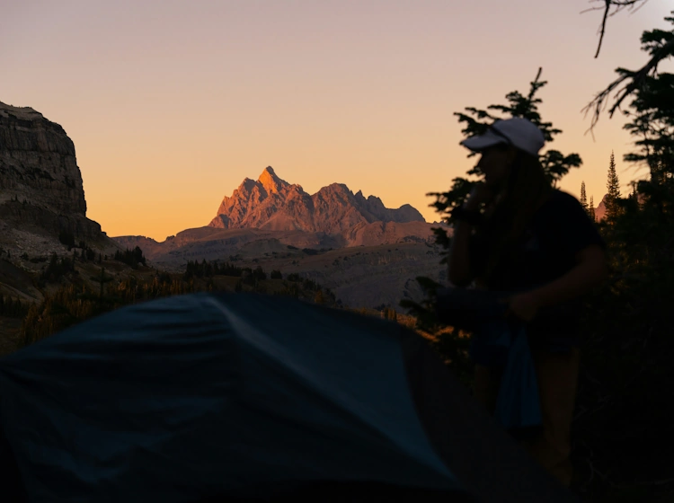 Lone camping tent at golden sunrise with dramatic mountain peaks